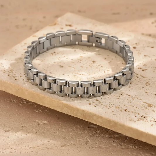 A silver stainless steel link bracelet displayed on a textured beige stone slab.