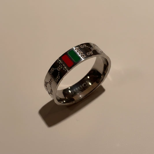 A silver-toned Gucci ring featuring the brand's signature GG monogram pattern and a green and red accent stripe, displayed on a beige surface.