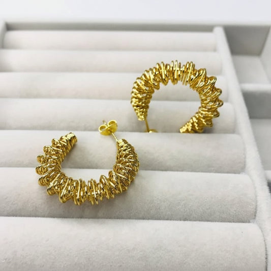 A pair of textured gold hoop earrings displayed on a white jewelry tray.