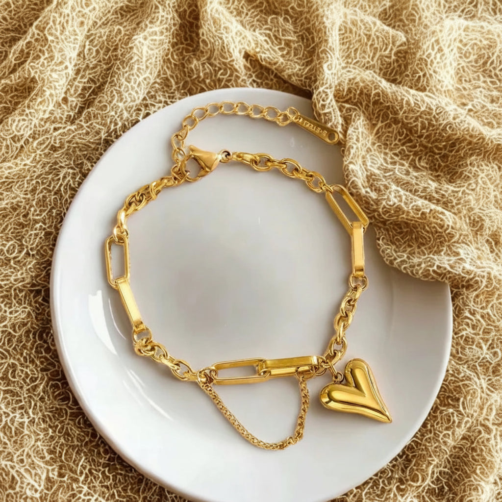 Gold bracelet with a heart charm on a white plate with a textured beige background