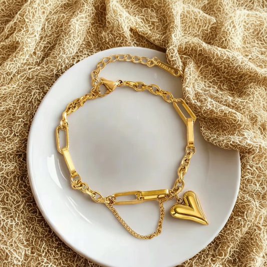 Gold bracelet with a heart charm on a white plate with a textured beige background