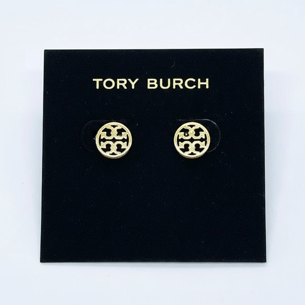 A pair of gold-tone Tory Burch stud earrings with a circular interlocking monogram logo, displayed on a white brand card.