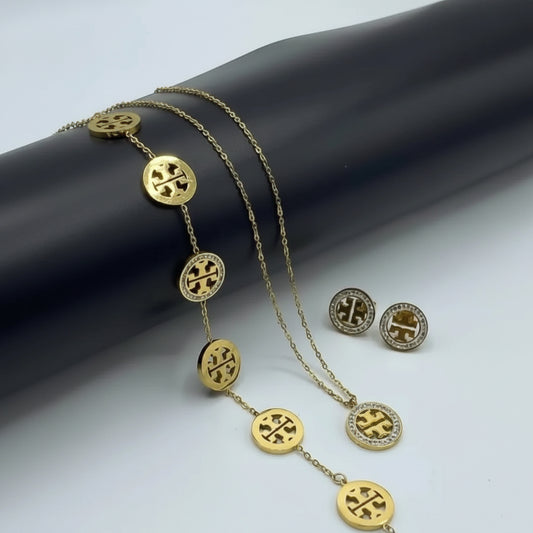 Gold-tone jewelry set featuring a chain bracelet, necklace, and stud earrings with circular logo medallions, displayed on a dark curved stand against a light background.