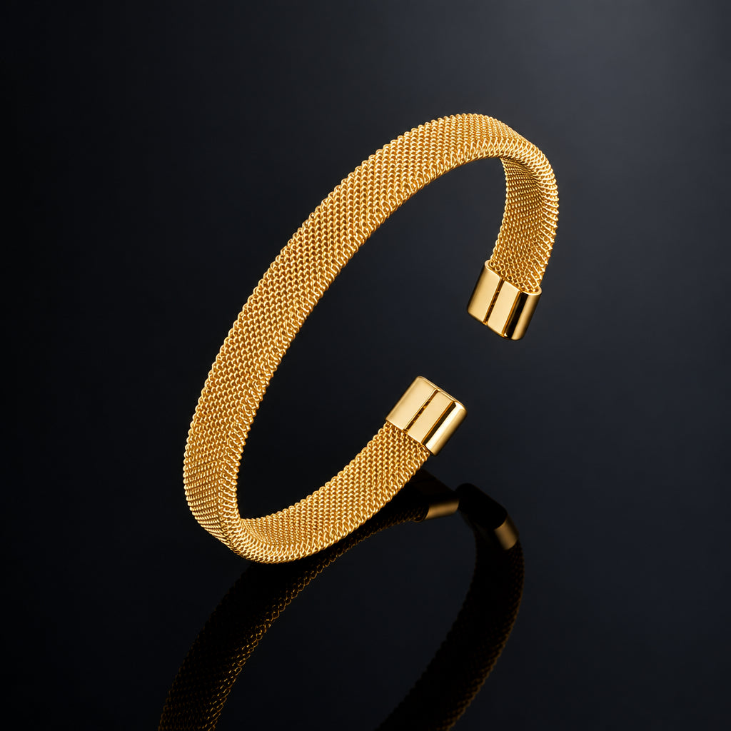 A gold-toned mesh cuff bracelet with polished end caps, displayed on a reflective dark surface against a black background.