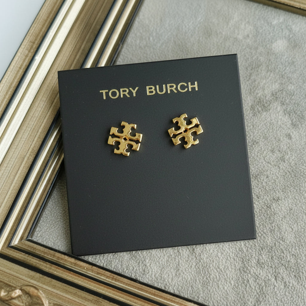 Gold earrings on a Tory Burch branded card against a textured surface